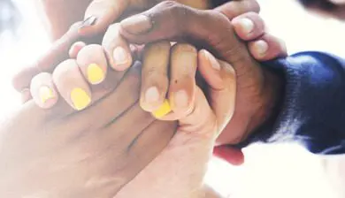 Close-up of diverse hands clasped together showing unity and support, with focus on the details of their interlocking fingers.