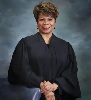 Portrait of a smiling woman wearing judicial robes against a mottled gray background.