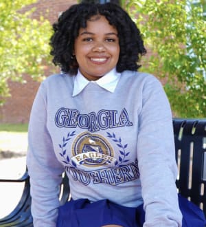 A young woman smiling, wearing a georgia southern sweater, sitting outdoors on a bench.