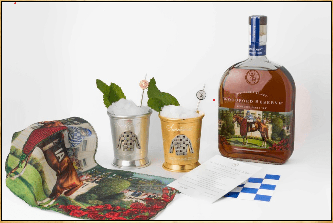 A display of woodford reserve bourbon, two mint julep cups with mint leaves, and derby-themed decorations, including a program and a pillow.