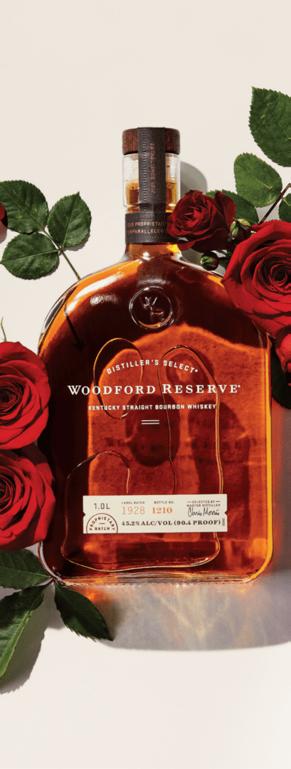 A bottle of woodford reserve bourbon surrounded by red roses on a white background.